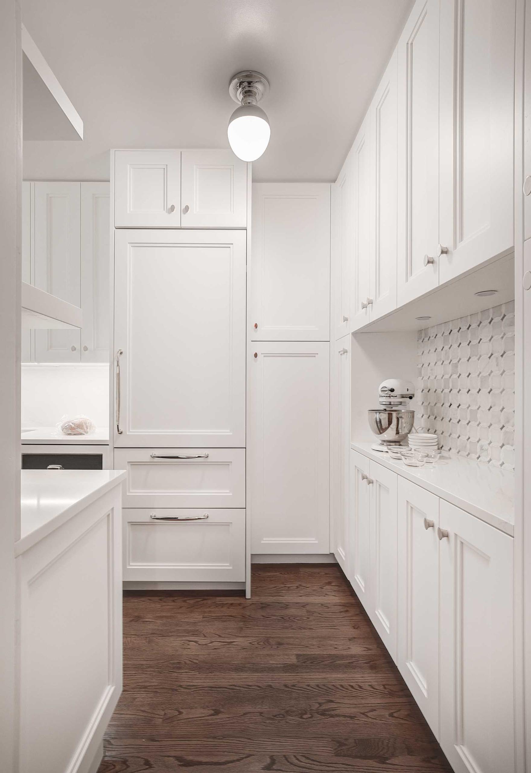 A contemporary kitchen with an integrated fridge, whose front matches the surrounding white cabinets.