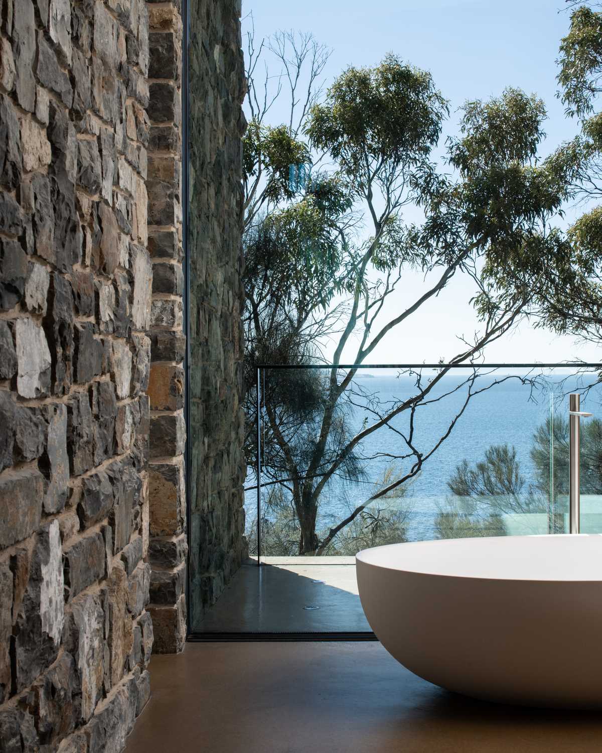 A modern bathroom with stone walls and floor to ceiling windows.