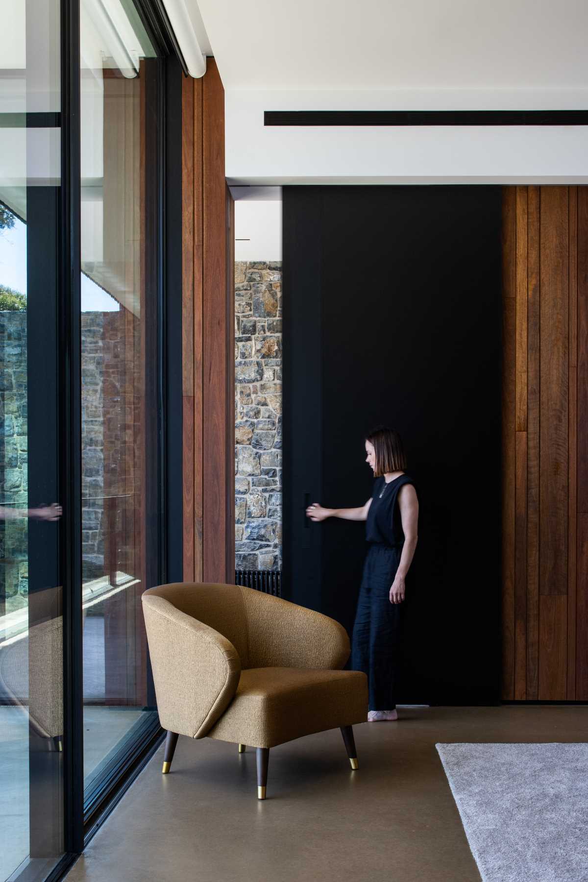 The oversized black pocket door of a bedroom in a modern house with stone walls.