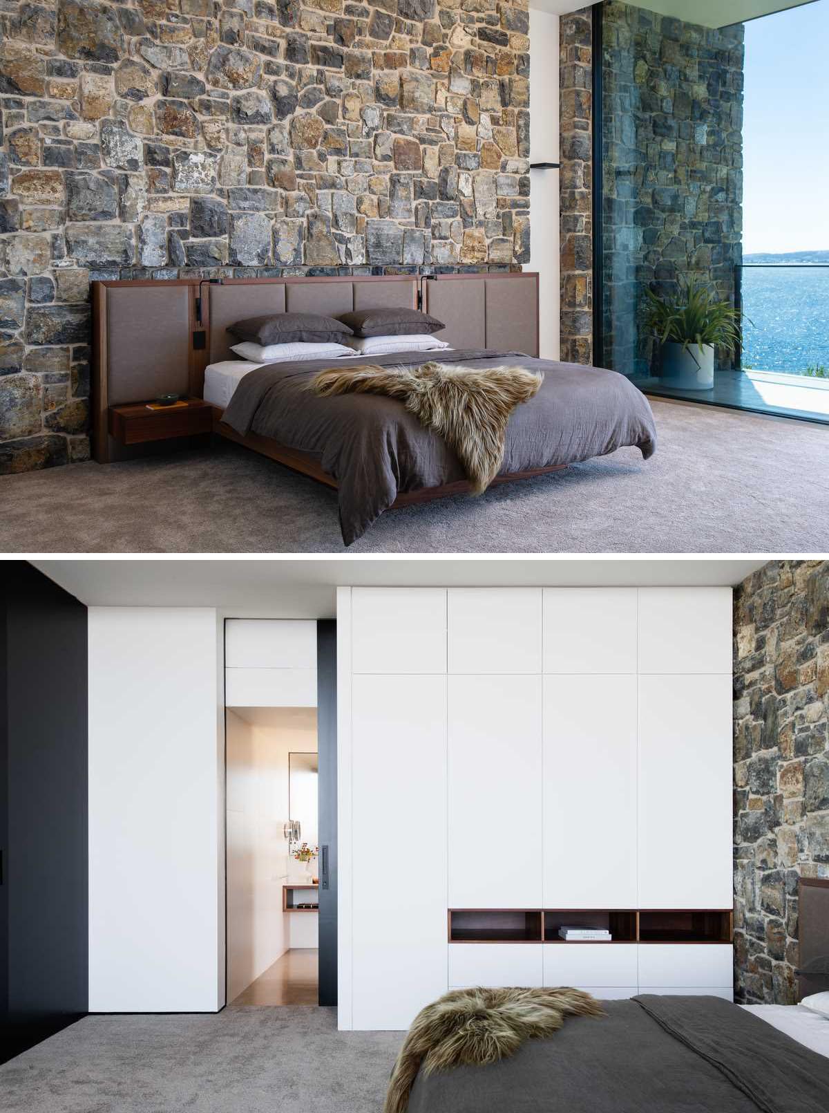 A modern bedroom with a stone wall behind the bed, a minimalist white closet, and black pocket door that opens to reveal the bathroom.