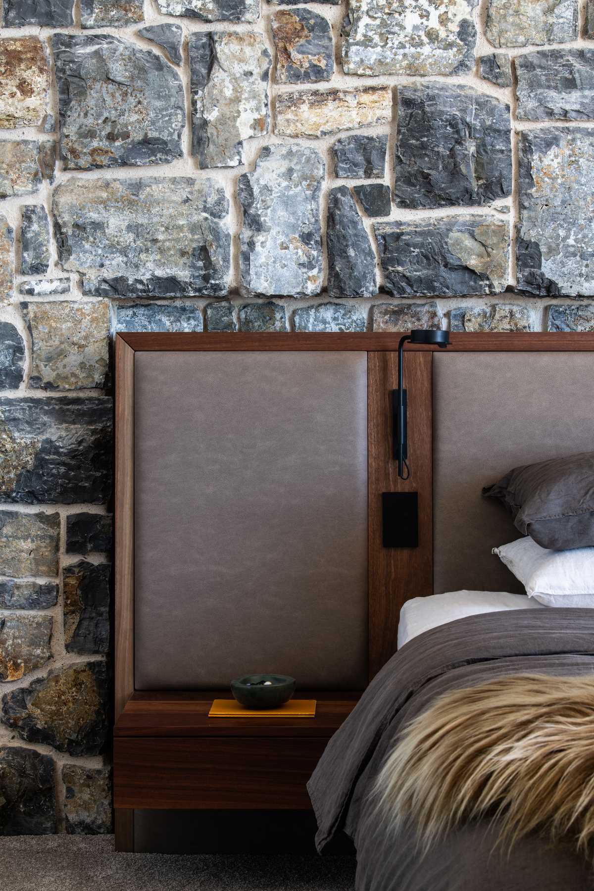 A modern bedroom with a stone wall behind the bed.