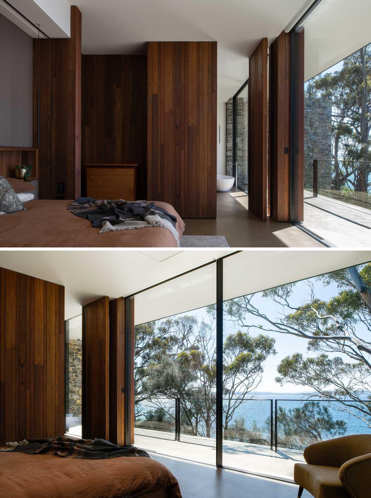 A modern bedroom with floor-to-ceiling windows, and a wood wall that includes a pivoting door that opens to reveal the bathroom.