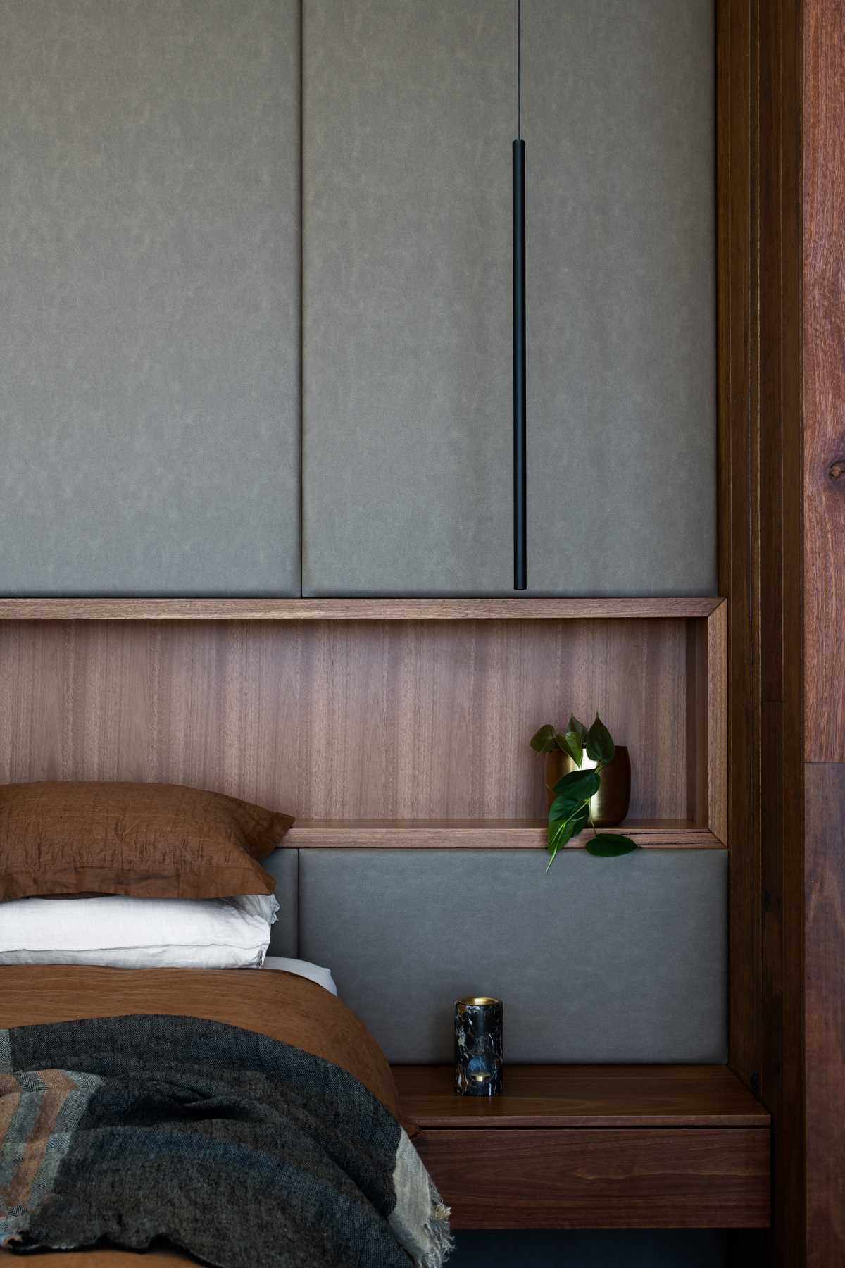 A modern bedroom with an upholstered accent wall that includes a shelving niche.