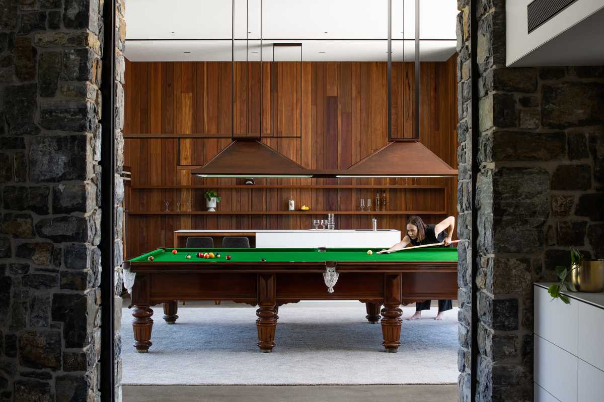 A games room has a warm atmosphere, with vertical wood strips creating an accent wall behind the bar.