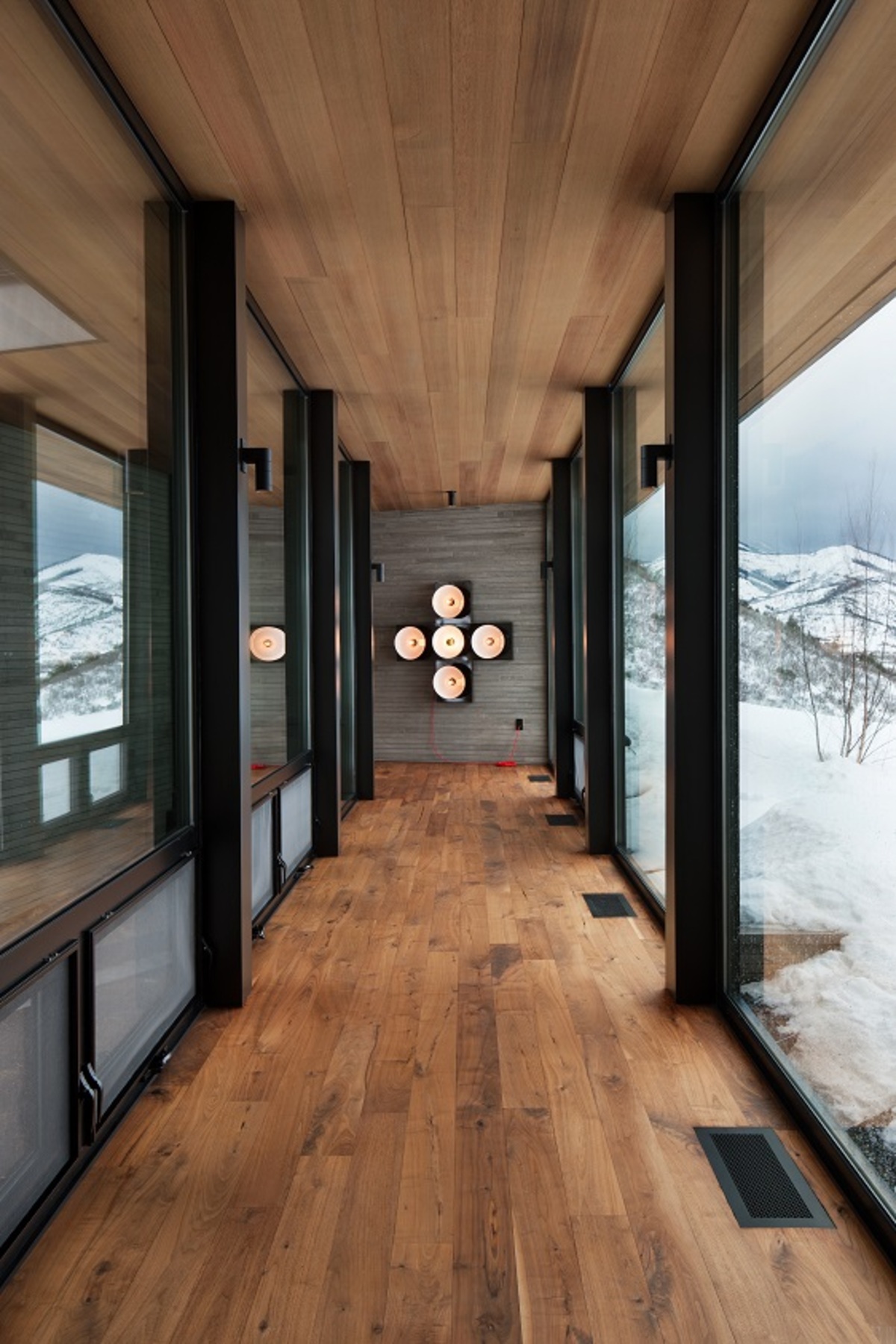 A modern hallway lined with glass walls also has a ceiling and floor lined with wood.