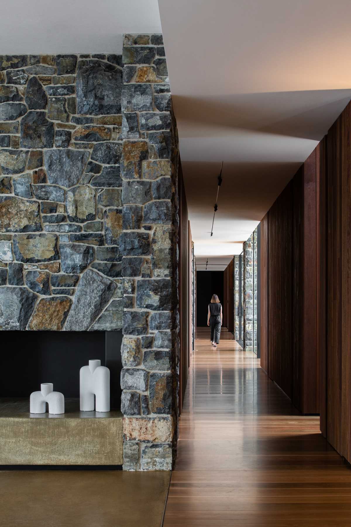 A modern hallway with wood floors, stone walls, and floor-to-ceiling windows.