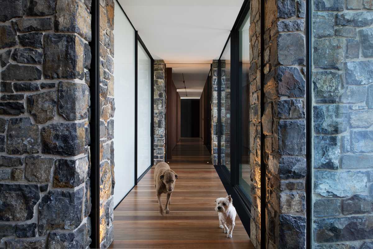 A modern hallway with wood floors, stone walls, and floor-to-ceiling windows.