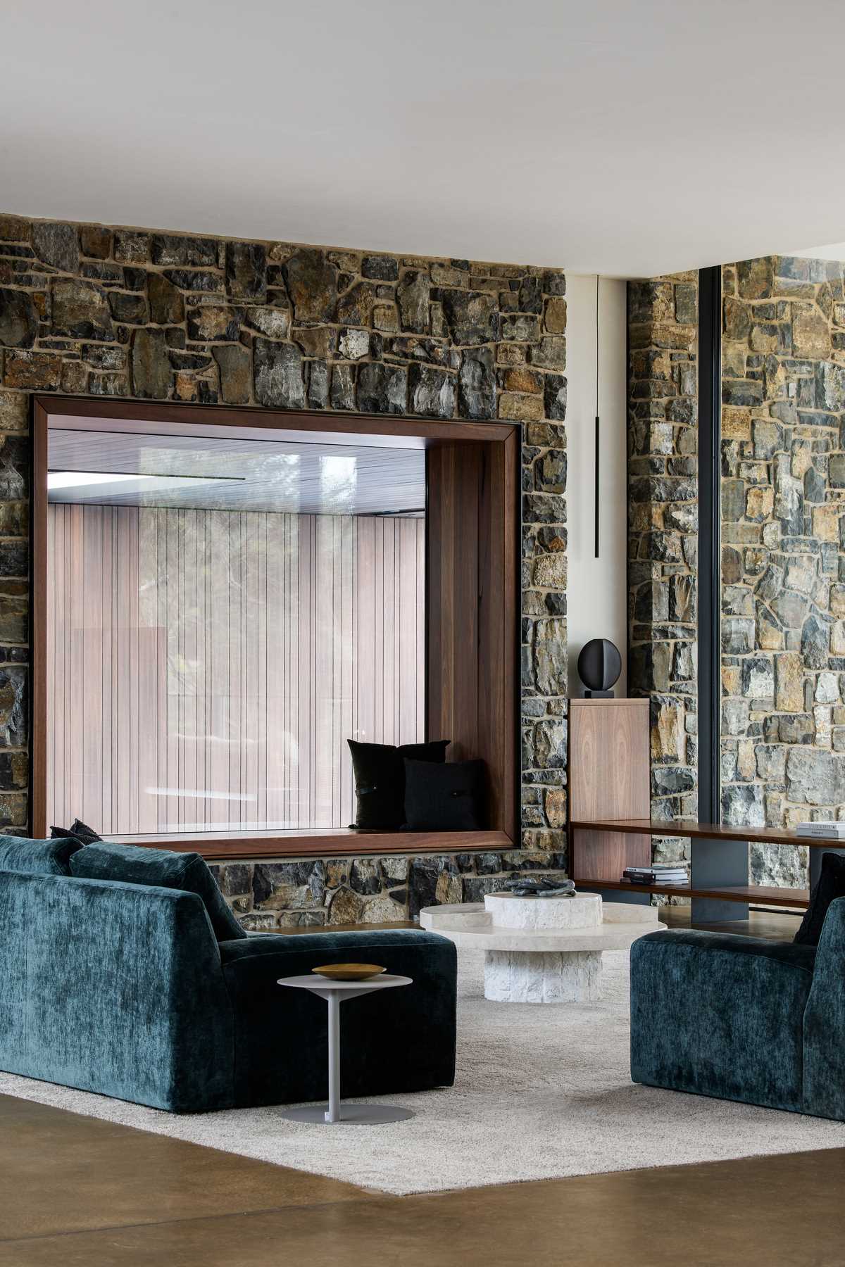 A modern living room with stone walls and a window seat that overlooks a swimming pool.