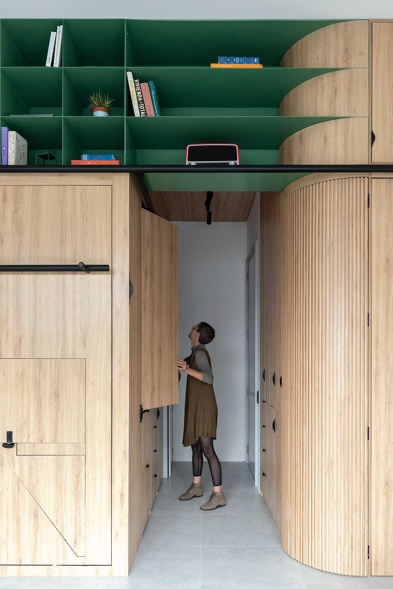 The small kitchen in this studio apartment is located in the hallway, where a folding cabinet door opens to showcase a contrasting dark kitchen countertop, sink, cooktop, and microwave.