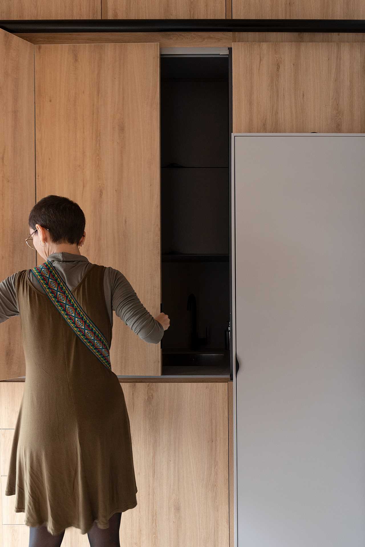 A small black kitchen is hidden behind cabinet doors in the hallway of this small apartment.