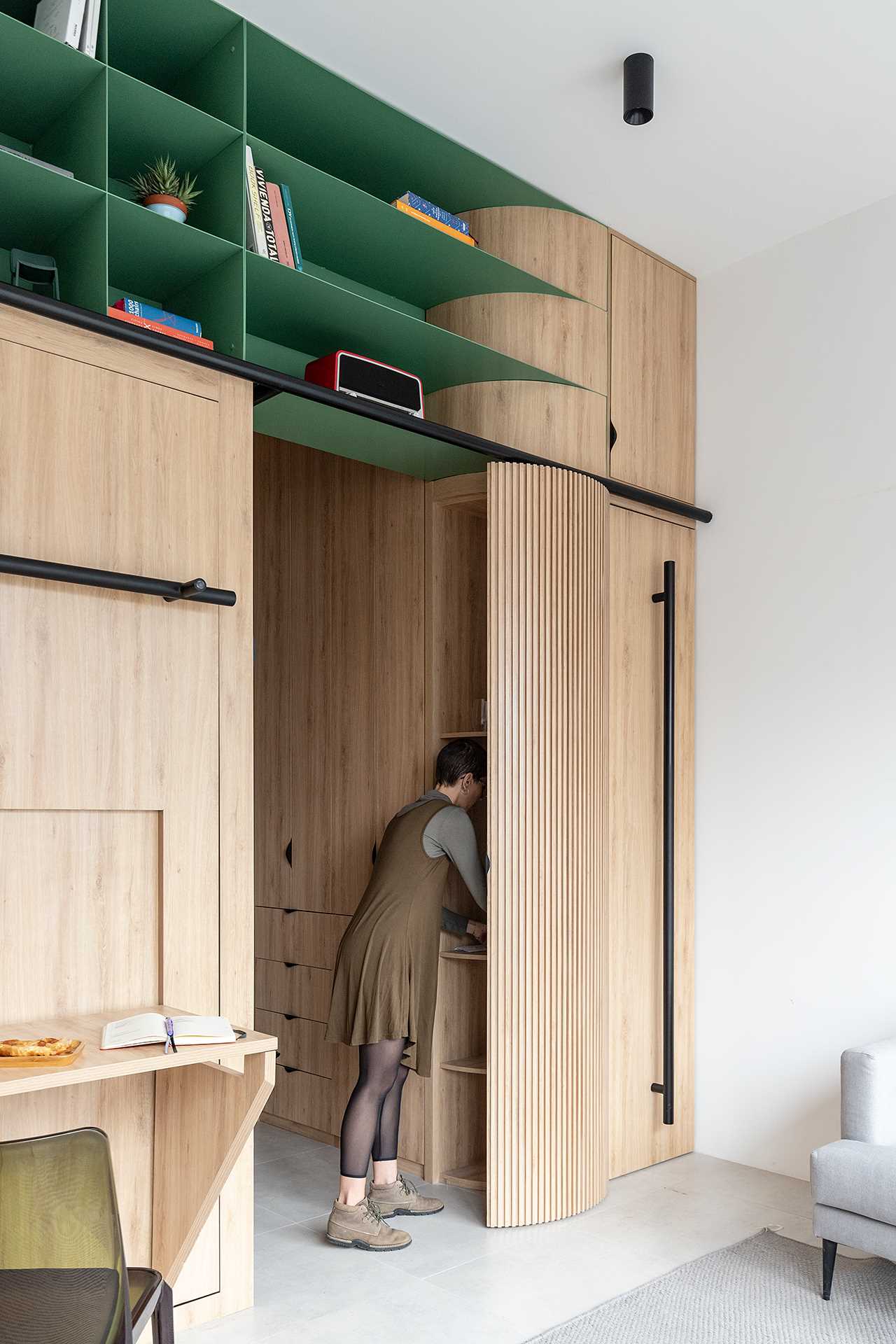 The corner of this small studio apartment has been softened with a curved cabinet that opens to shelving.