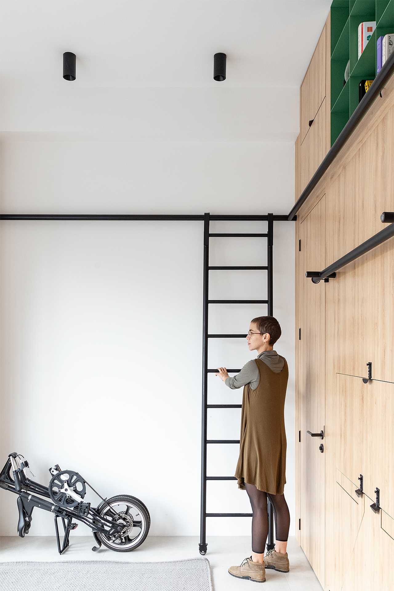 A studio apartment includes a black metal ladder that allows the apartment owner to easily access the upper storage cabinets.