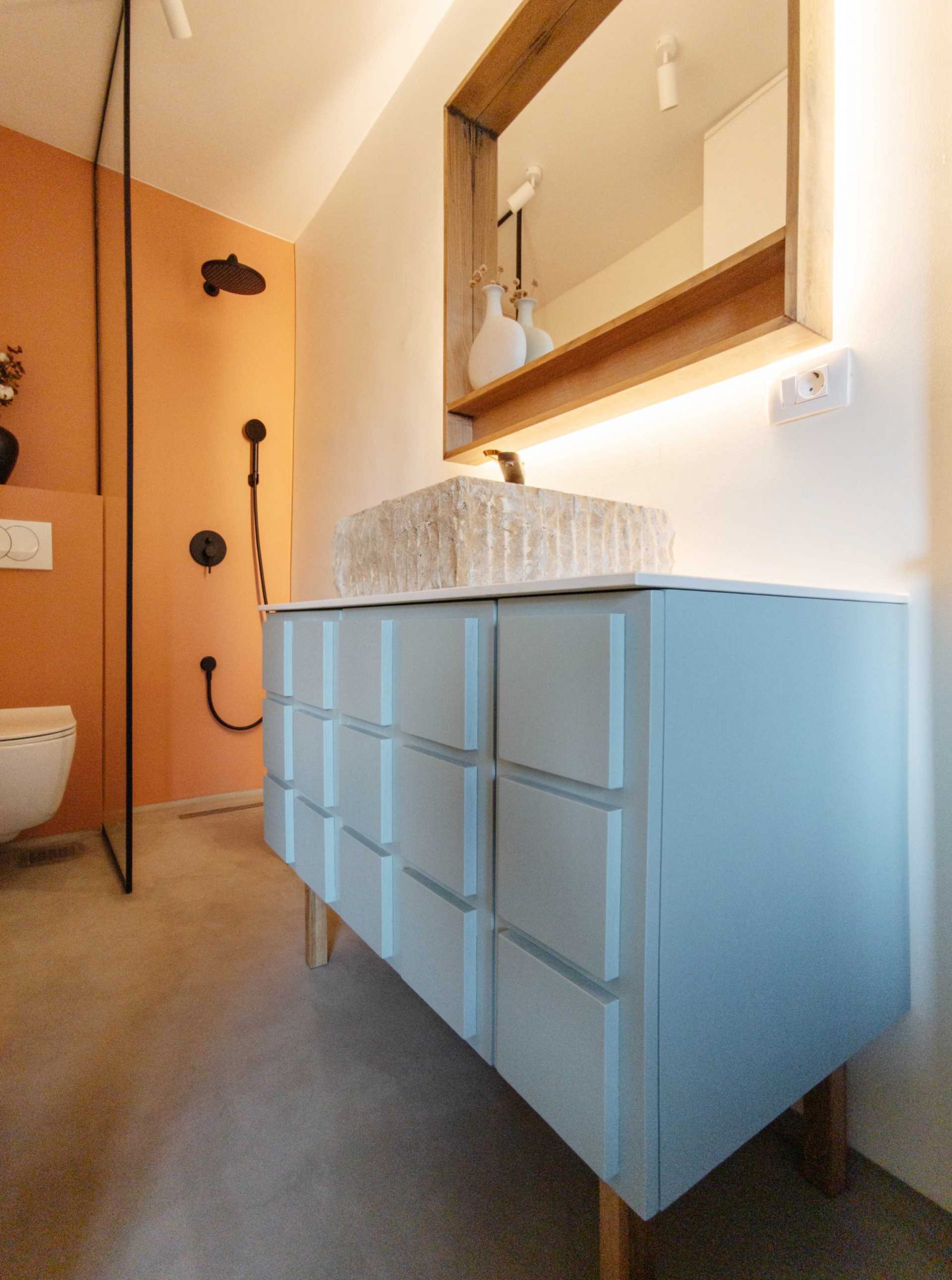 A contemporary bathroom with a matte orange accent wall, and a blue bathroom vanity with a carved sink.