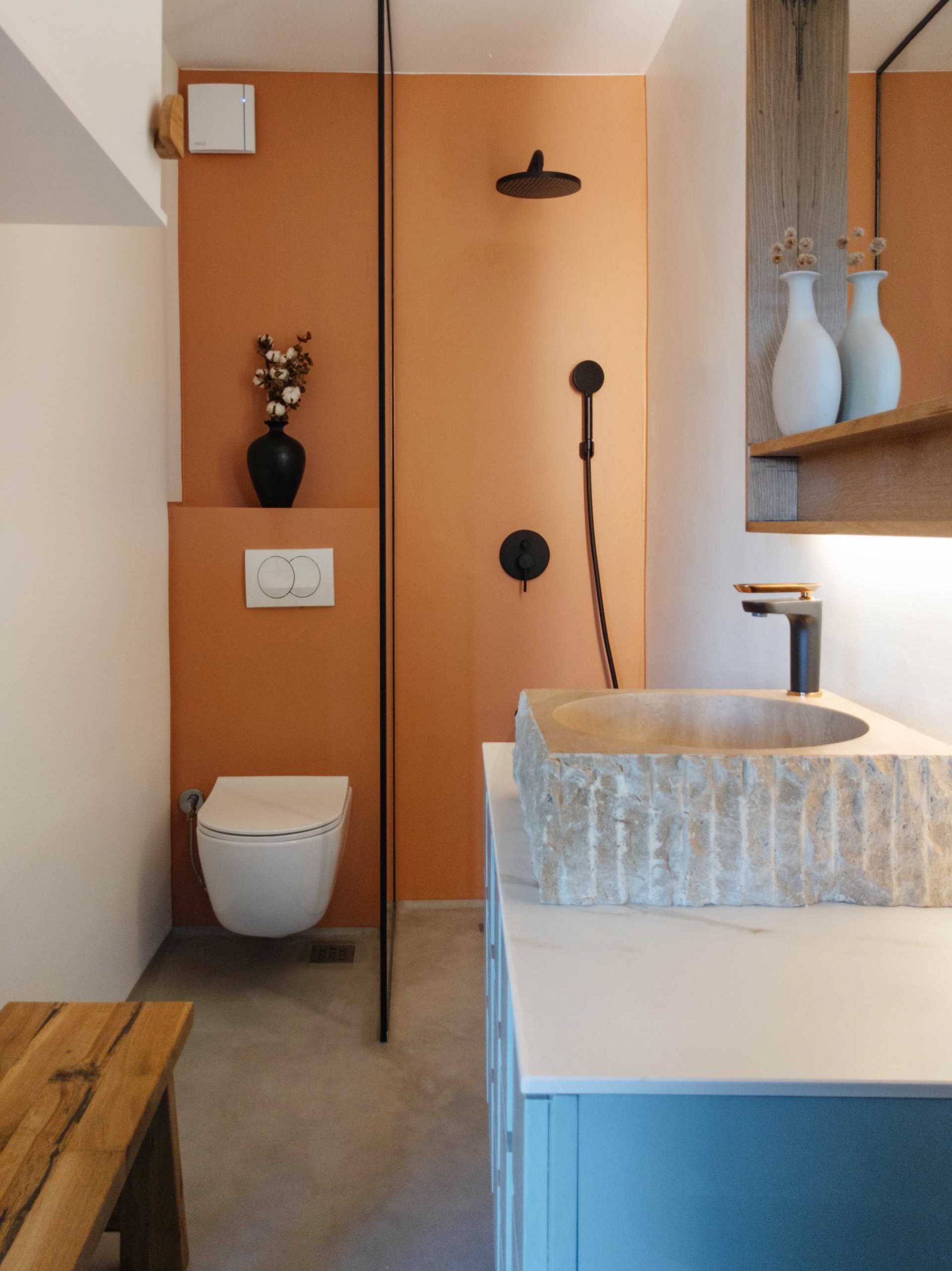 A contemporary bathroom with a matte orange accent wall, and a blue bathroom vanity with a carved sink.