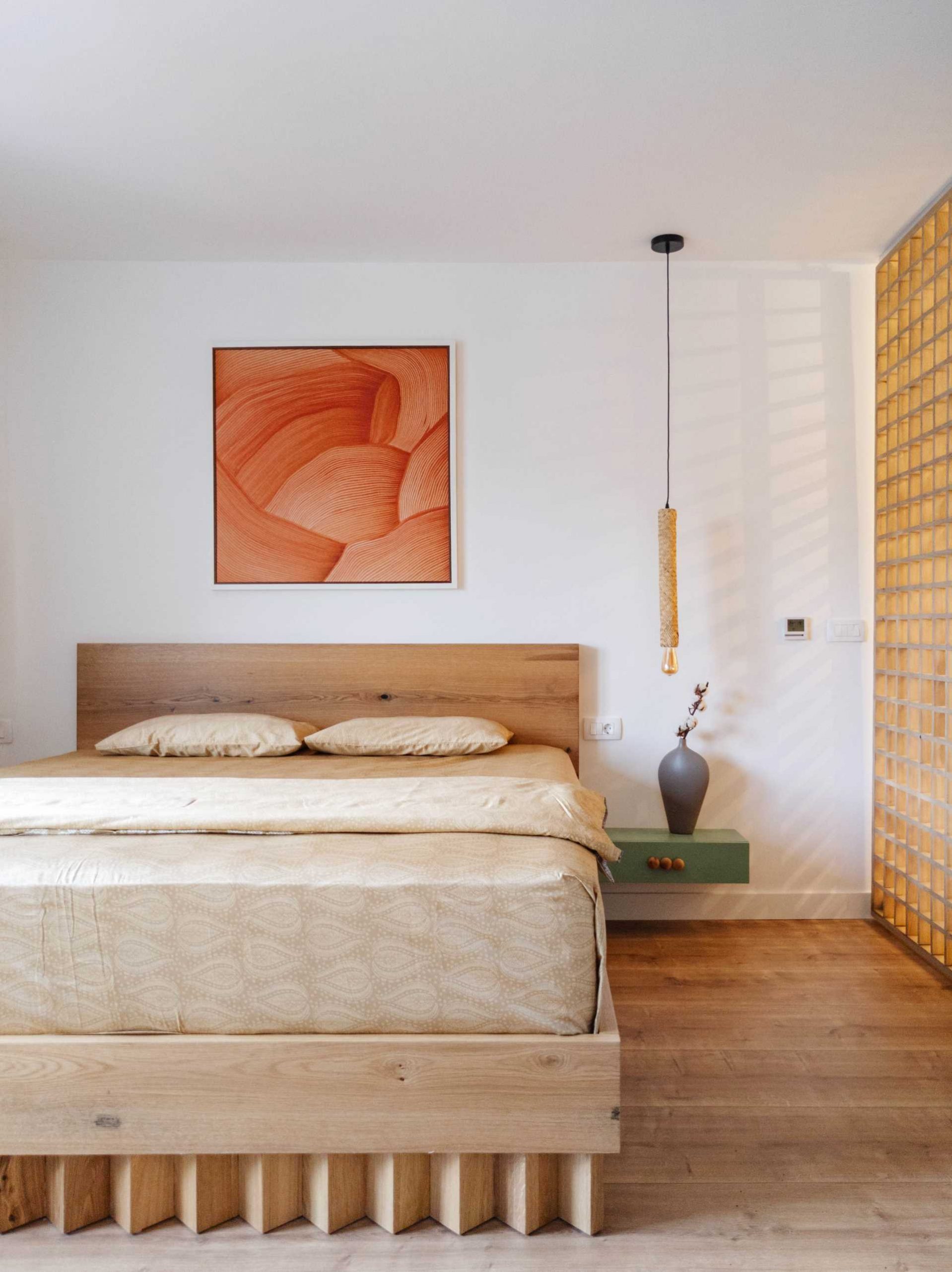 In the bedroom, there's a geometric wood accent that covers the wall, while the a wood bed frame has a unique design for it's base. A floating matte green bedside table has a design that matches the nearby vanity.