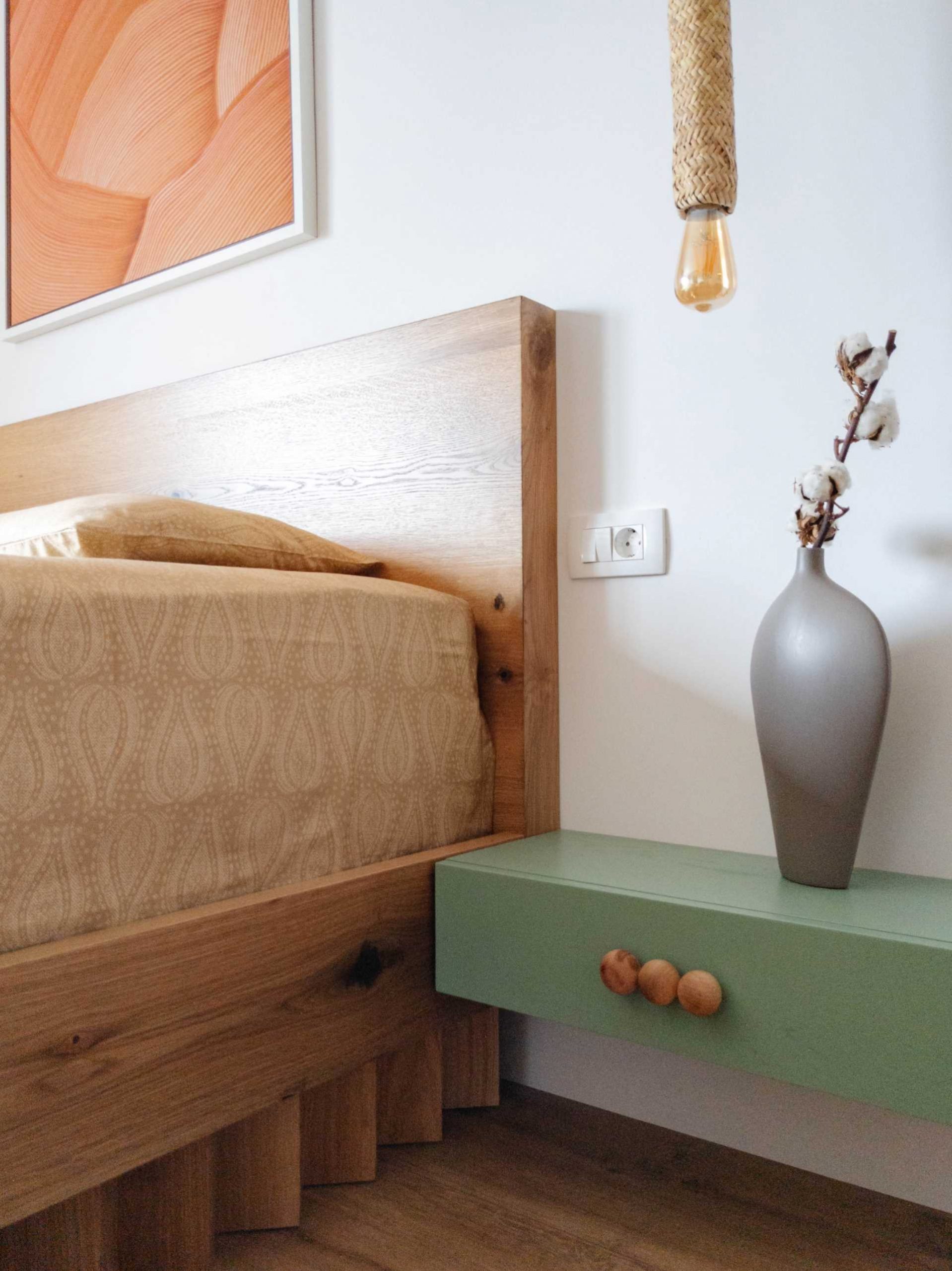 A contemporary bedroom with a wood bed frame and matte green floating bedside table.