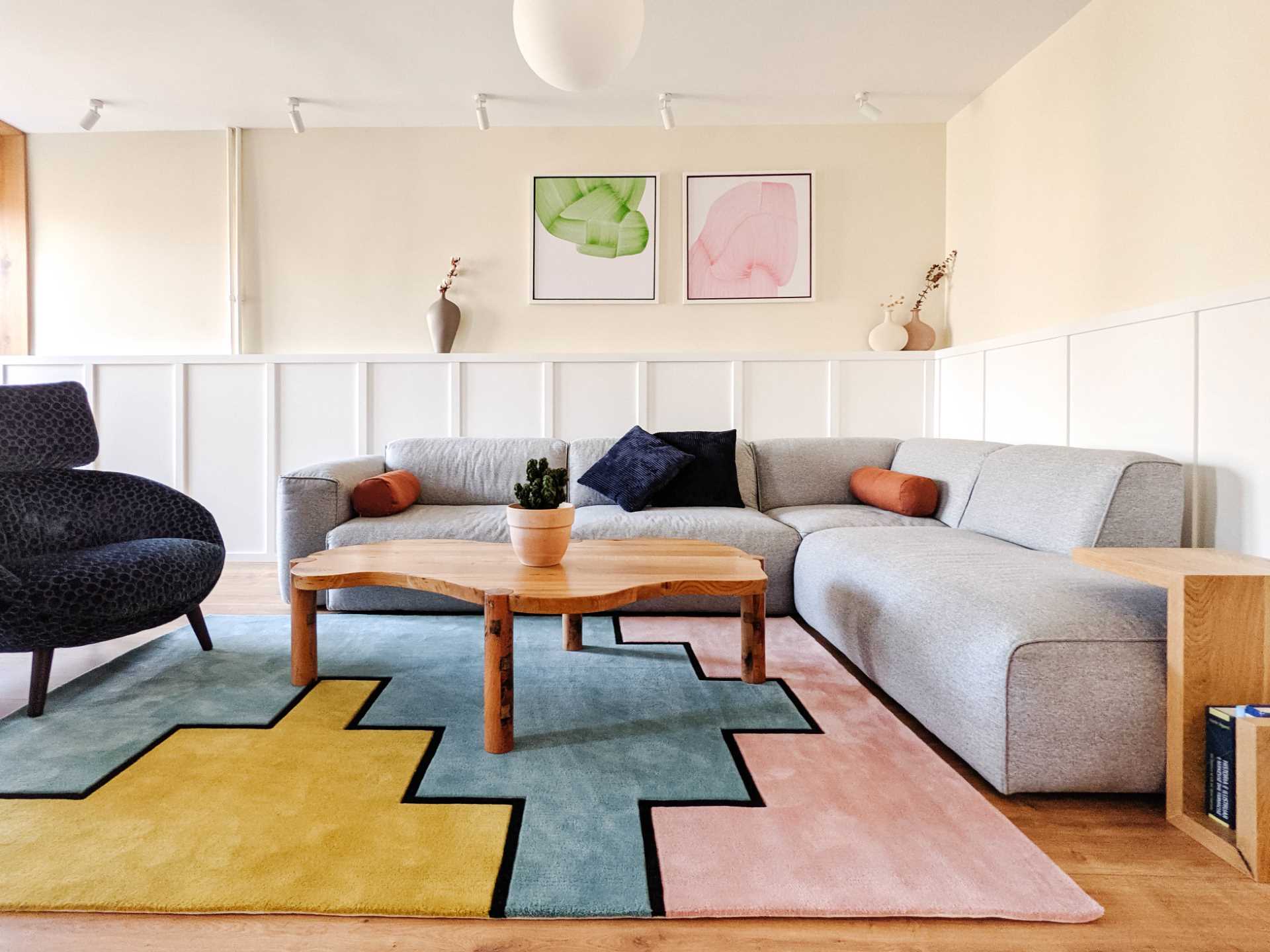 In this contemporary living room, wainscoting lines the wall, and a colorful geometric rug complements the artwork on the wall.