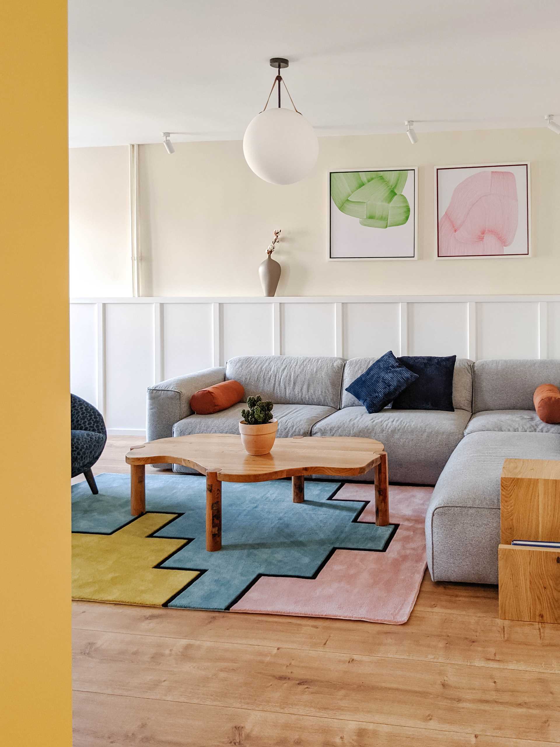 In this contemporary living room, wainscoting lines the wall, and a colorful geometric rug complements the artwork on the wall.