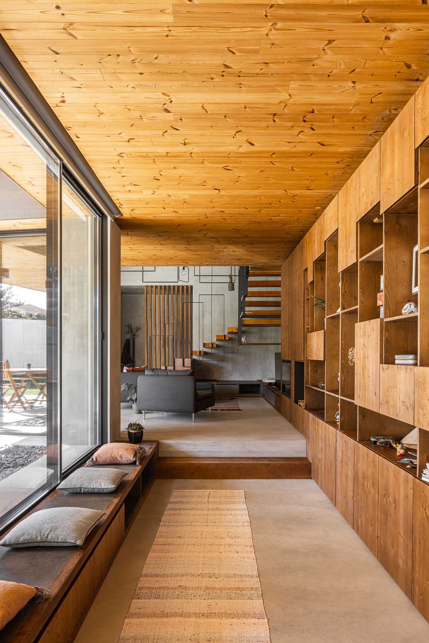 Một hành lang hiện đại với giá sách bằng gỗ có thang và băng ghế bên cửa sổ.