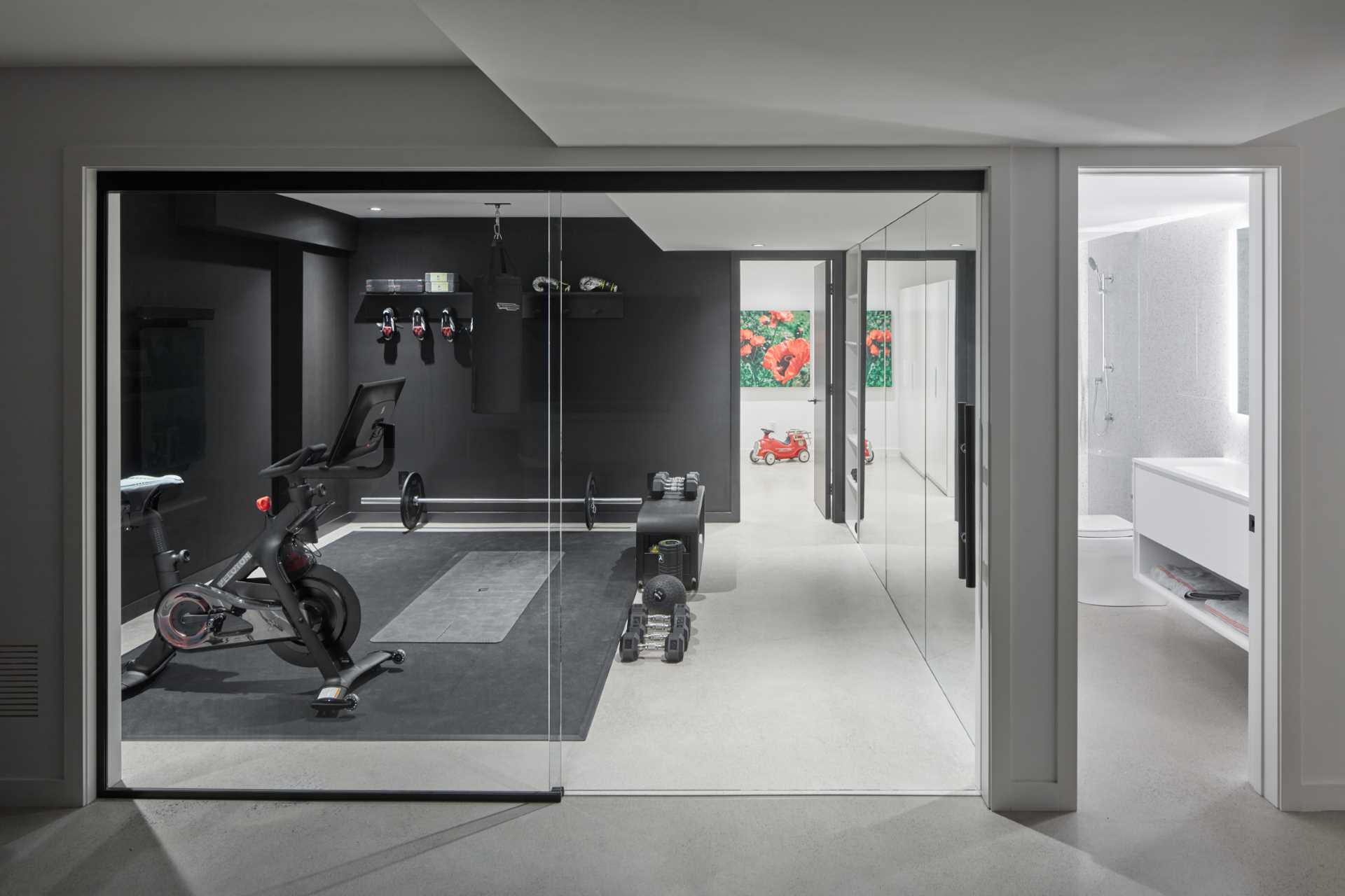 The basement level of this modern home has a gym with a mirrored wall and black accent walls.