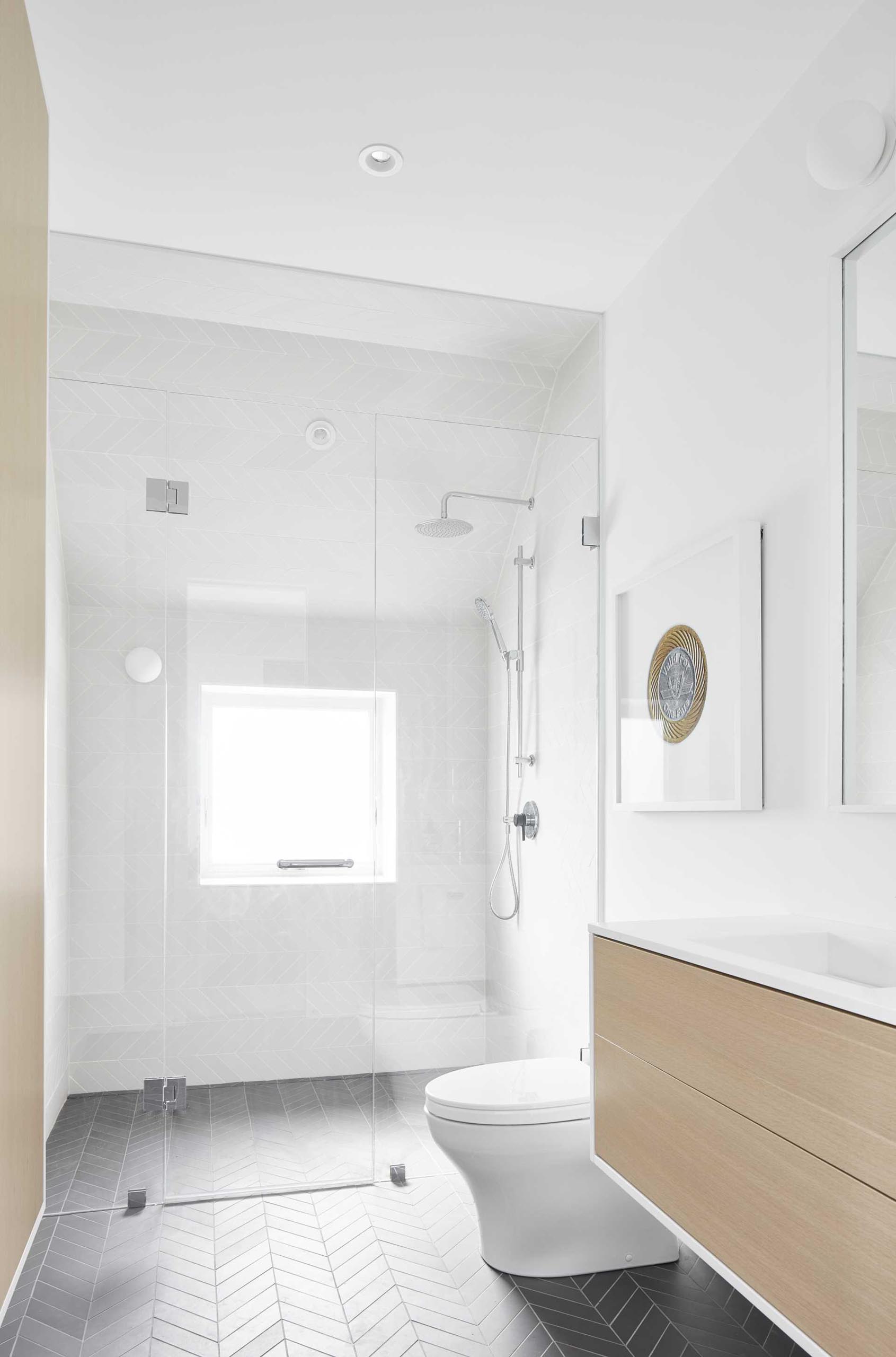 In this modern guest bathroom, the color palette has been kept simple, with white walls and wall tiles, white oak vanity, and dark tiles in a chevron pattern.