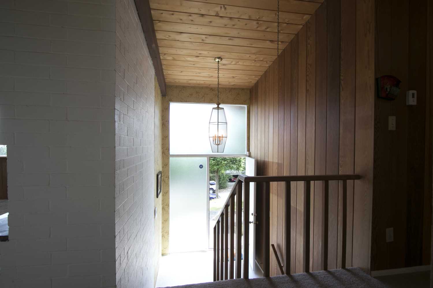 BEFORE - The original entryway of the home had dark wood paneling on the wall, wallpaper, and lighter wood on the ceiling. 