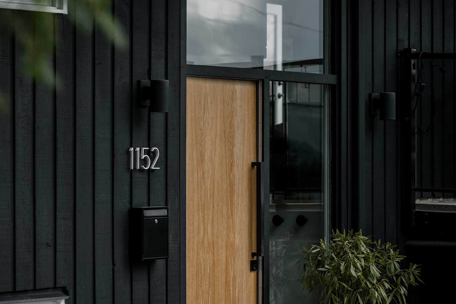 A remodeled home includes black painted wood exterior and a light wood front door.