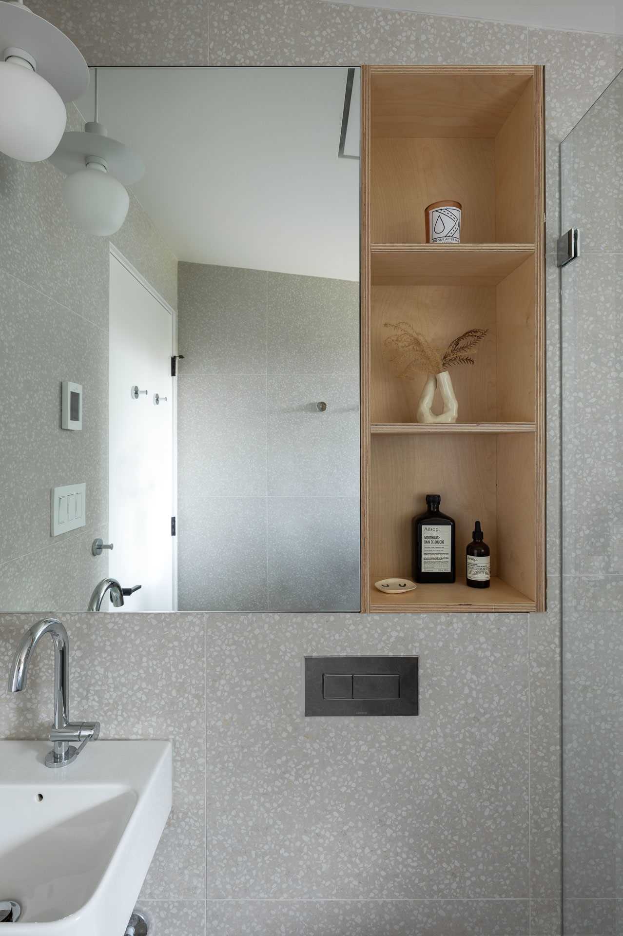 A remodeled bathroom with terrazzo wall tiles and plywood shelving.