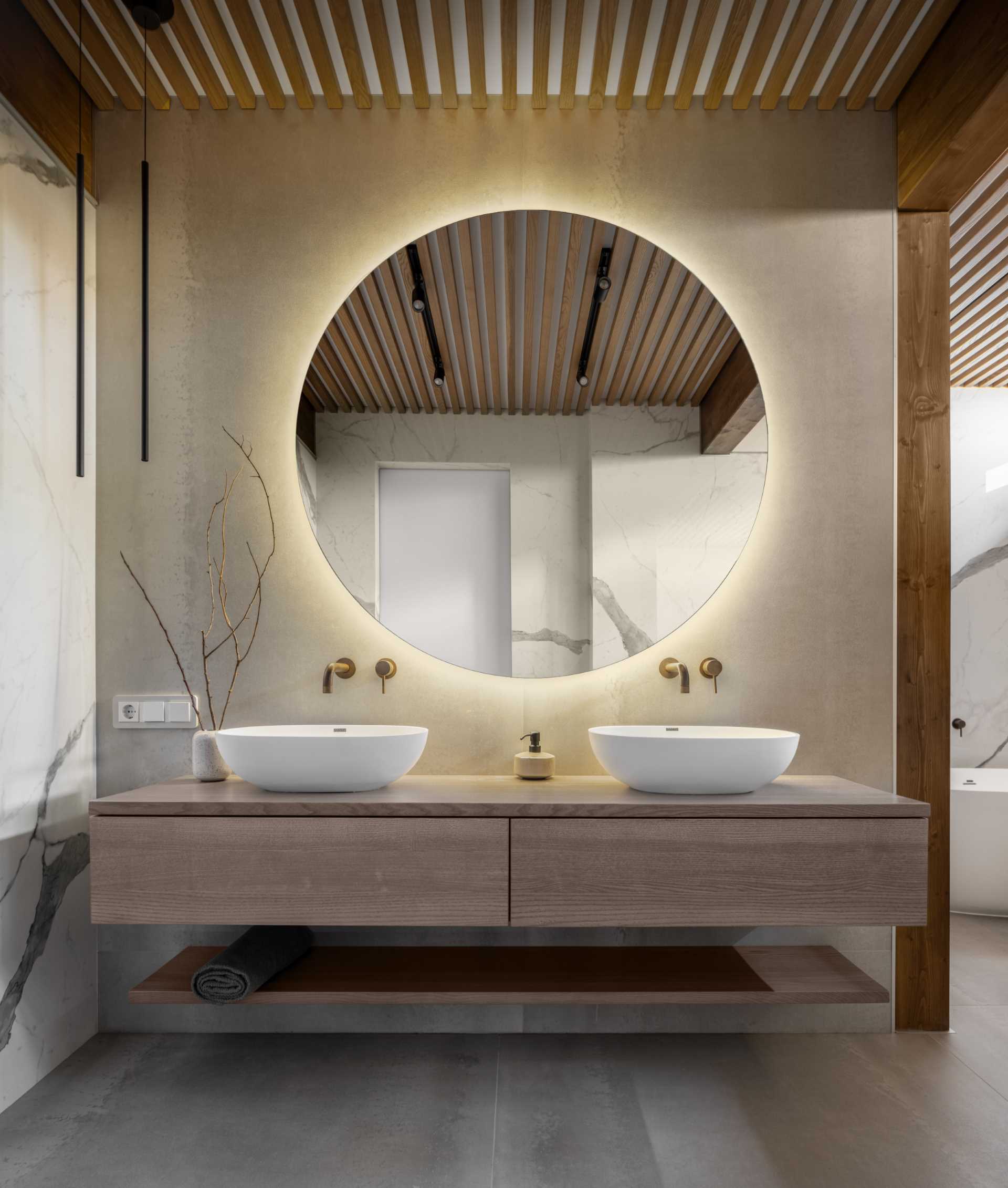 A modern bathroom with a floating wood vanity and a round backlit mirror.