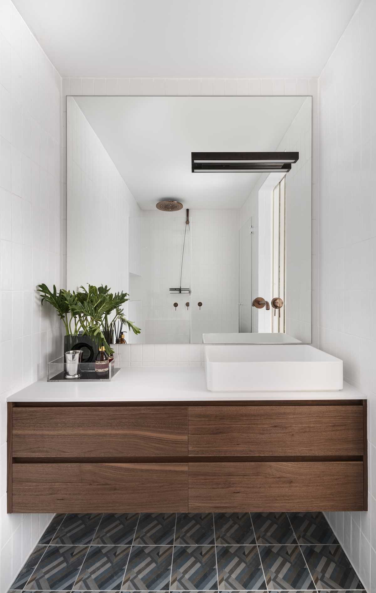 This modern bathroom has a full-width floating wood vanity, tiled walls, and a patterned floor.
