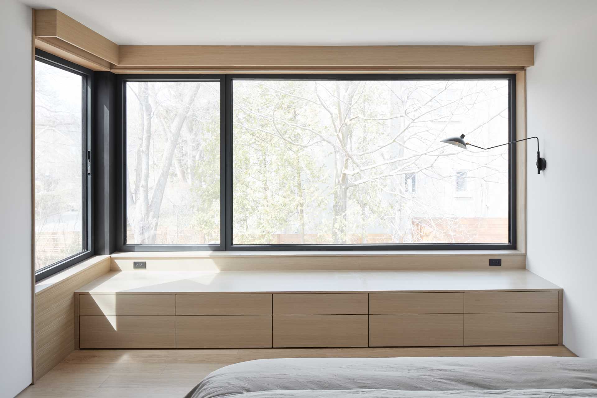 A modern bedroom includes a built-in window bench and black window frames that complement the black wall-mounted light.