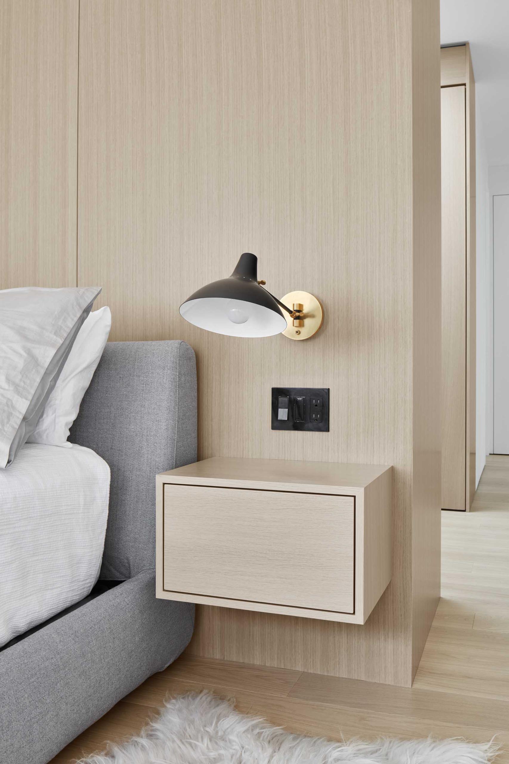 This modern primary bedroom has a white oak accent wall behind the bed, with matching floating bedside tables.