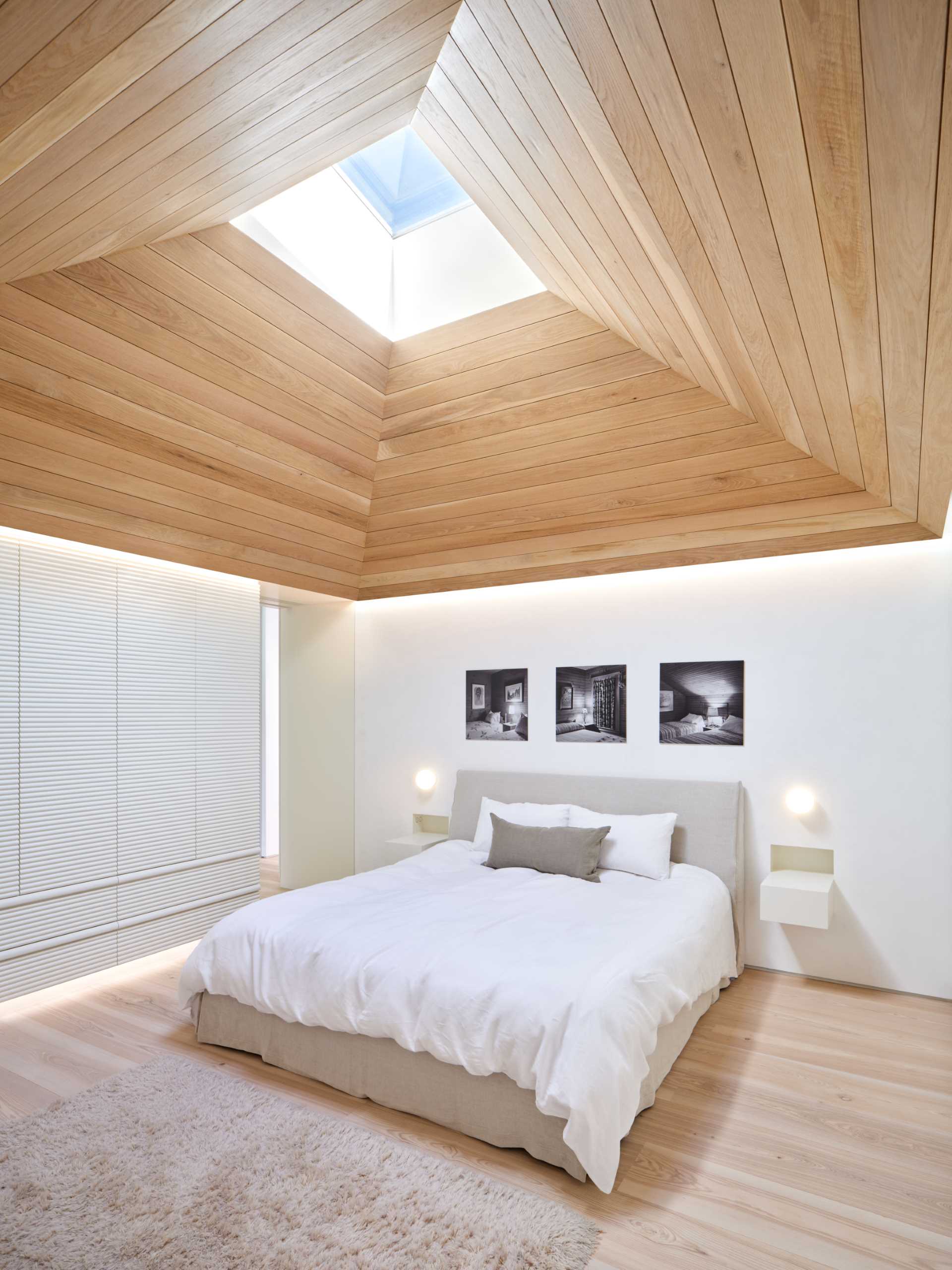 This modern primary bedroom is characterized by a white oak vaulted ceiling whose skylight pulls morning light down into the space. 