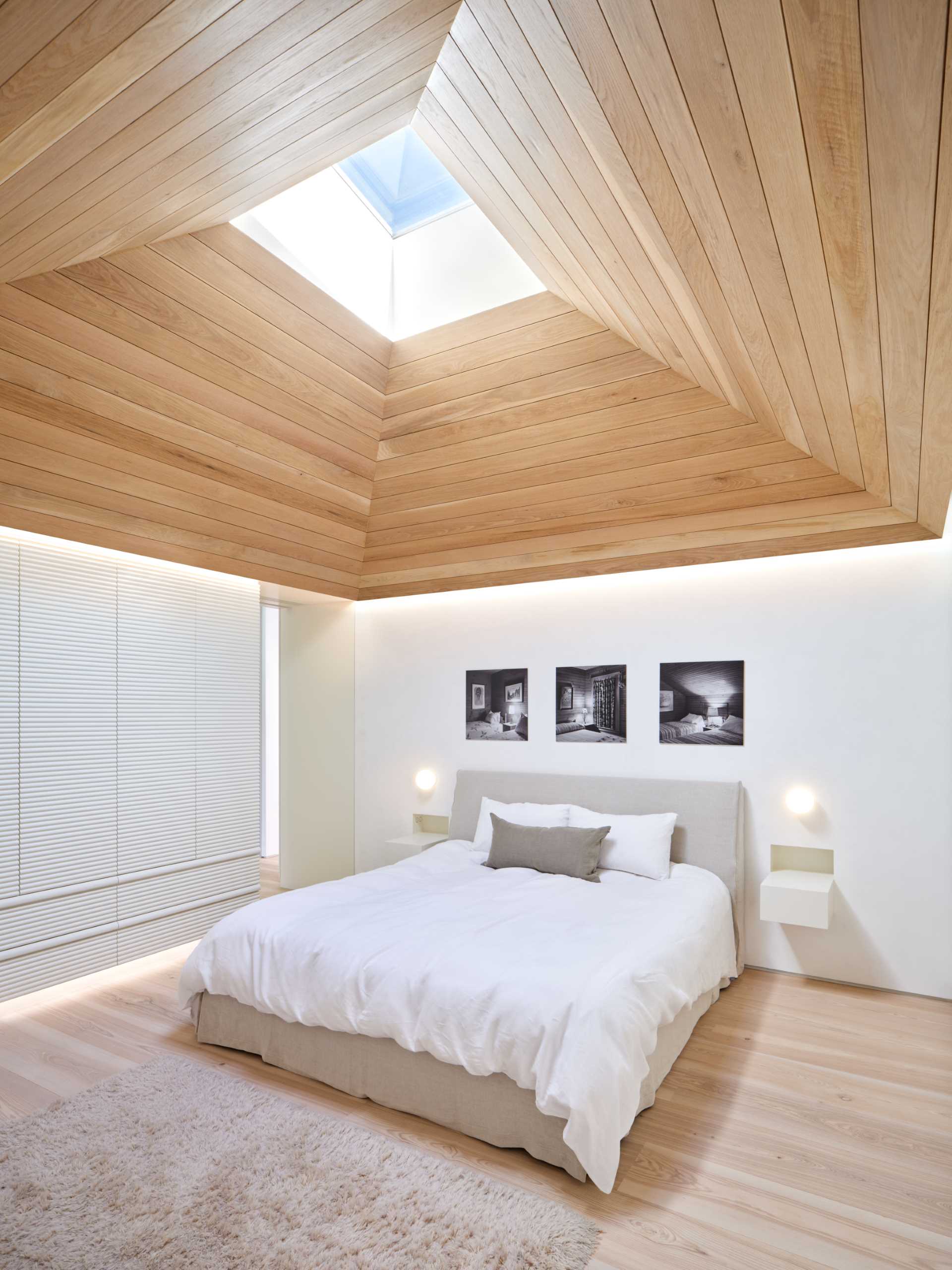 This modern primary bedroom is characterized by a white oak vaulted ceiling whose skylight pulls morning light down into the space.