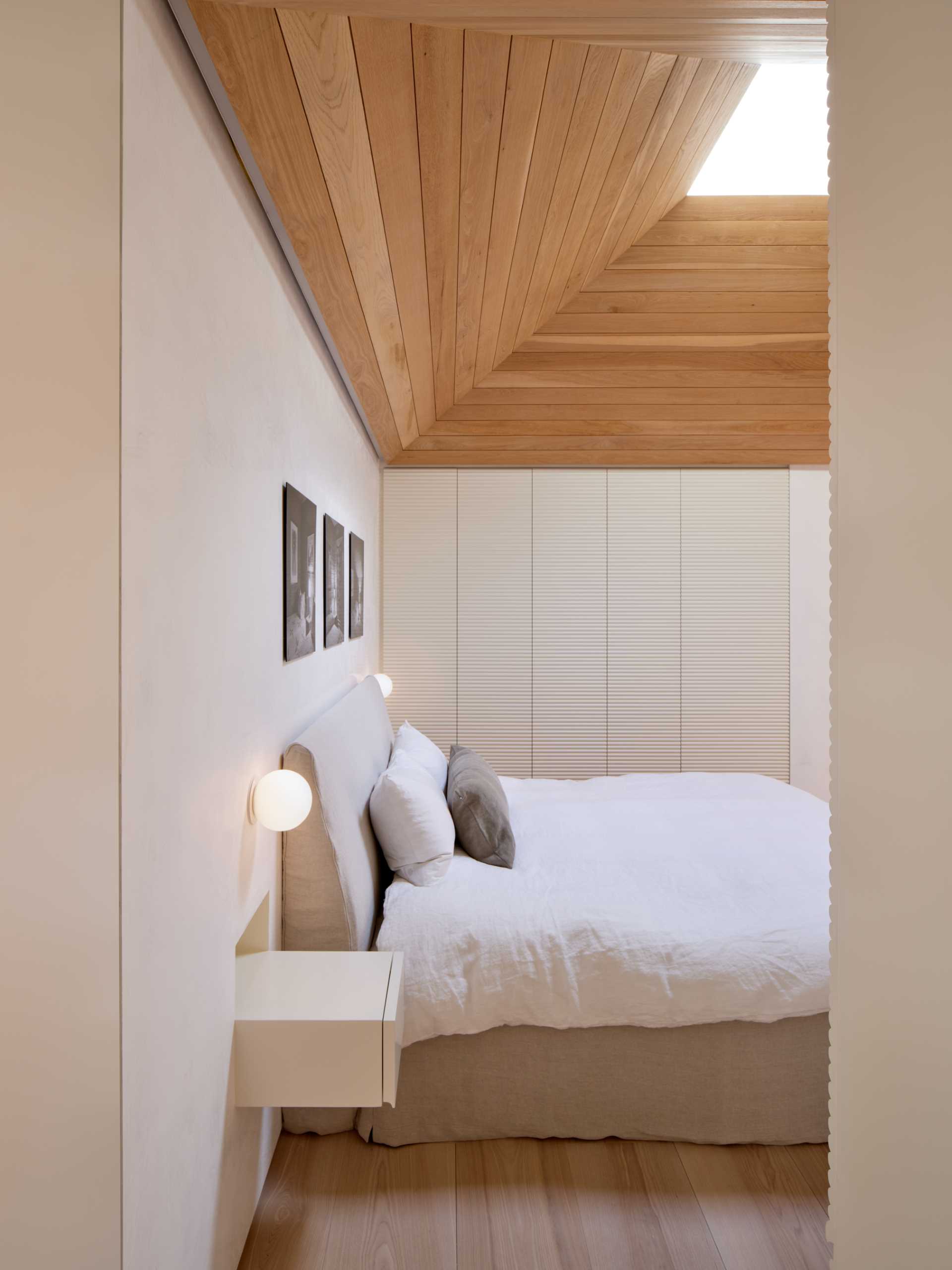 This bedroom has a white oak vaulted ceiling whose skylight pulls morning light down into the space. 
