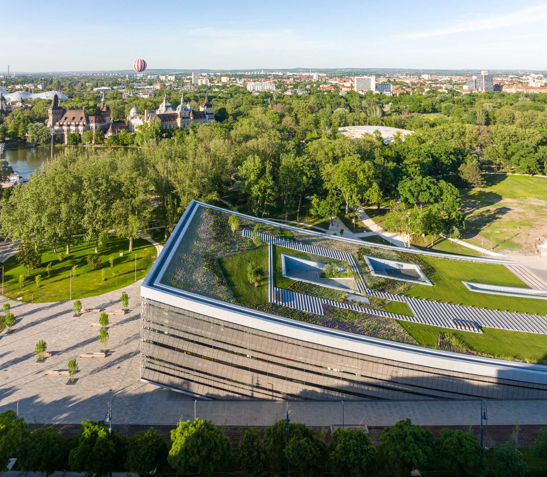 A modern building with a curved green roof includes grass, plants, and steps.