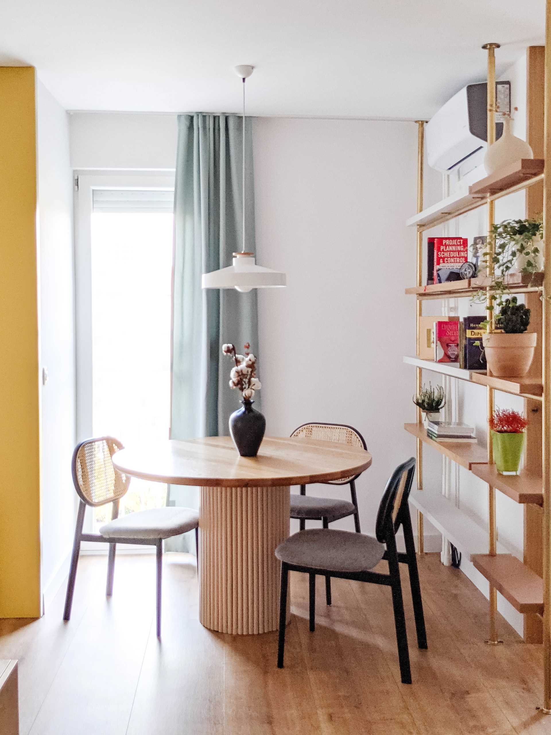 A contemporary dining room with a round table and a metal shelving unit with wood shelves.