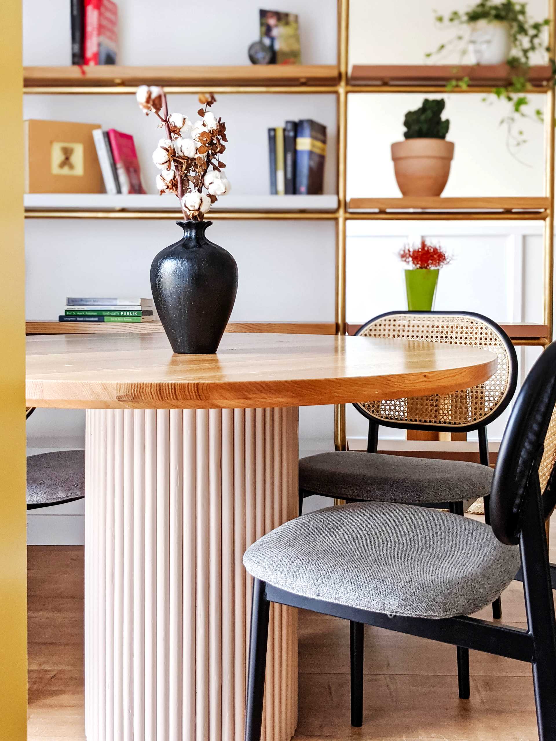 A contemporary dining room with a round table and a metal shelving unit with wood shelves.