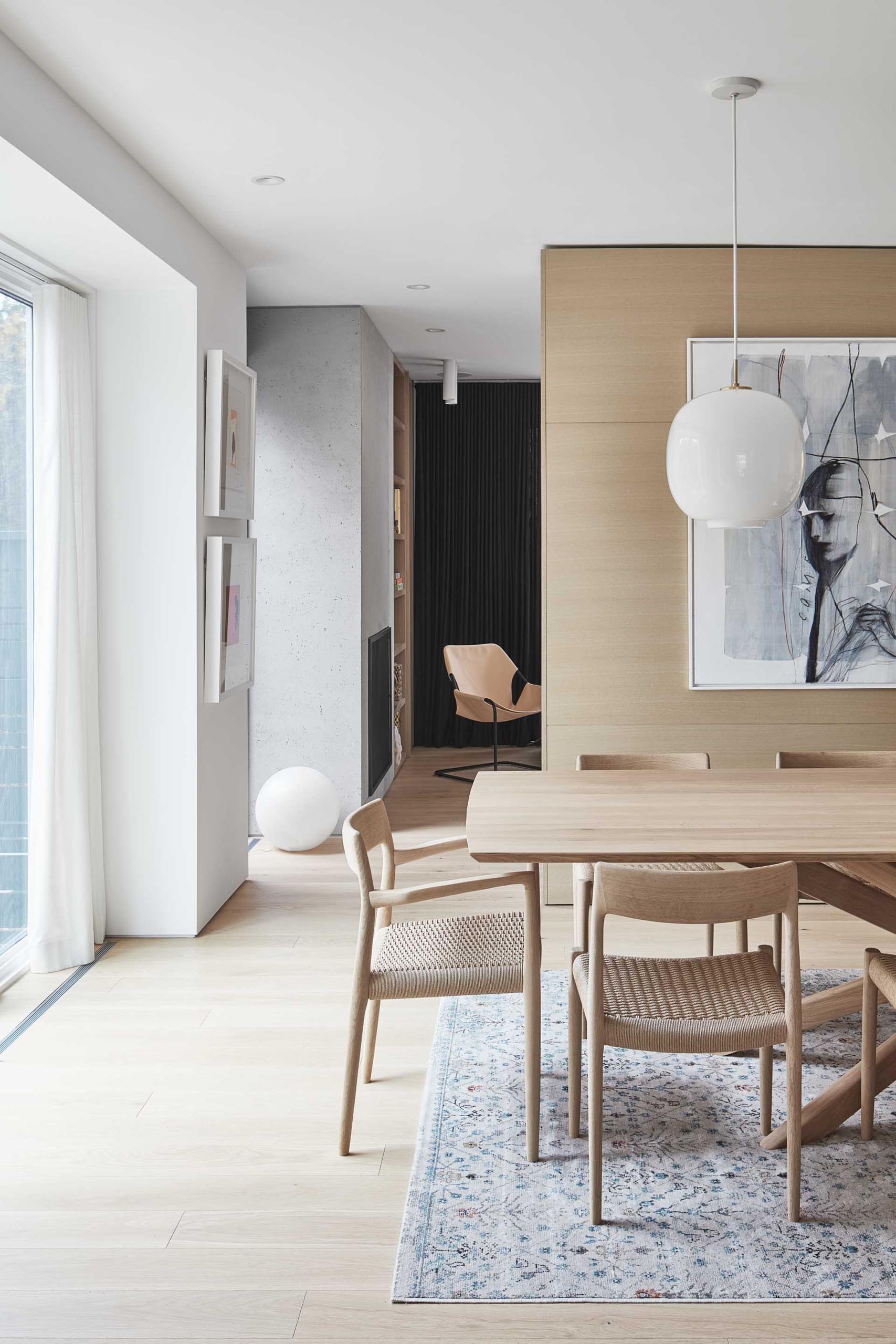 This open plan dining room, includes a large wood table and matching chairs, two simple white pendant lights hang above the table for a contemporary look.