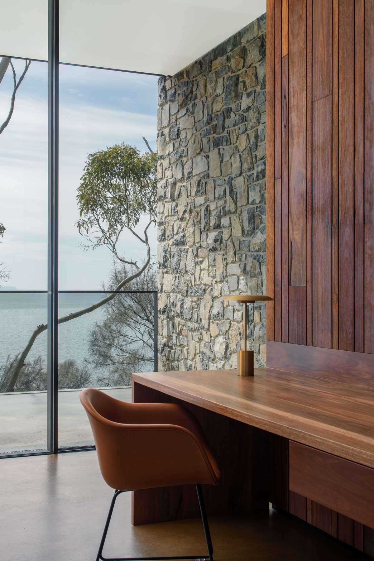 A modern home with stone and wood walls, floor-to-ceiling windows, and a built-in wood desk.