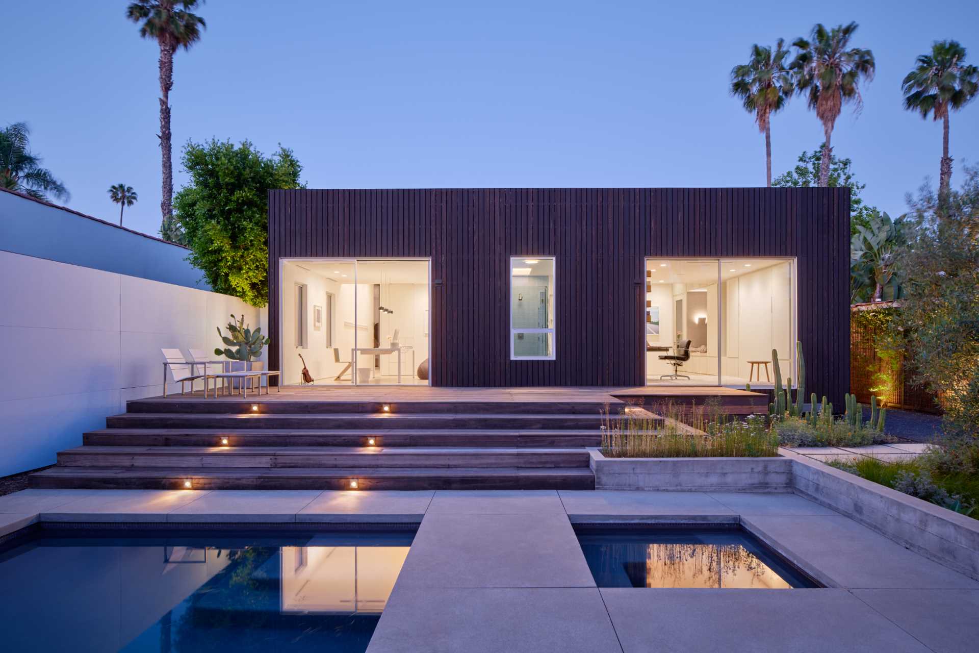 At the rear of this modern home, there's a wood deck that steps down to a small pool and hot tub. Small dedicated planters are filled with easy-to-care for plants.