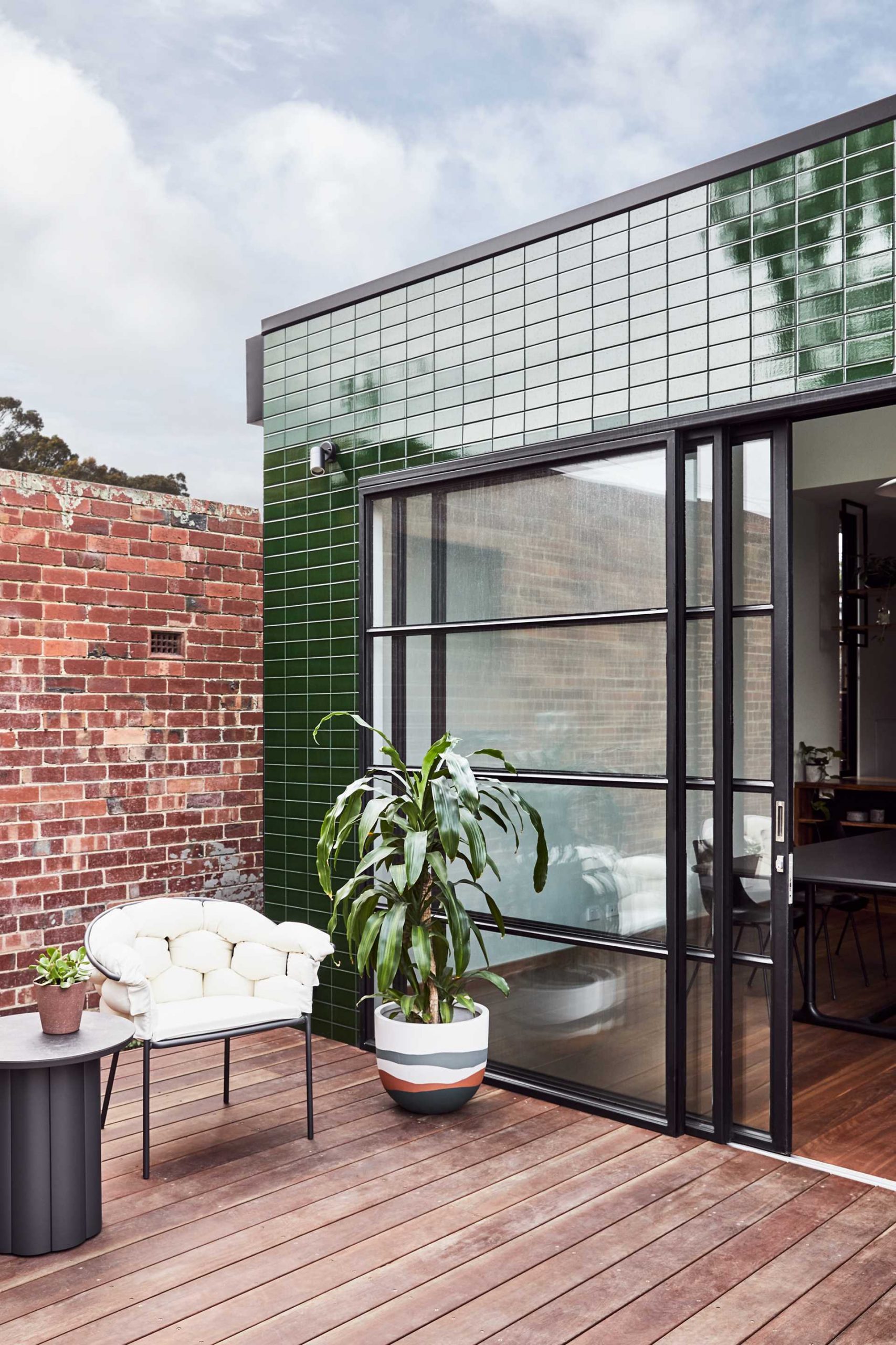 A modern house extension with glazed green tiles and black steel framed sliding glass door.