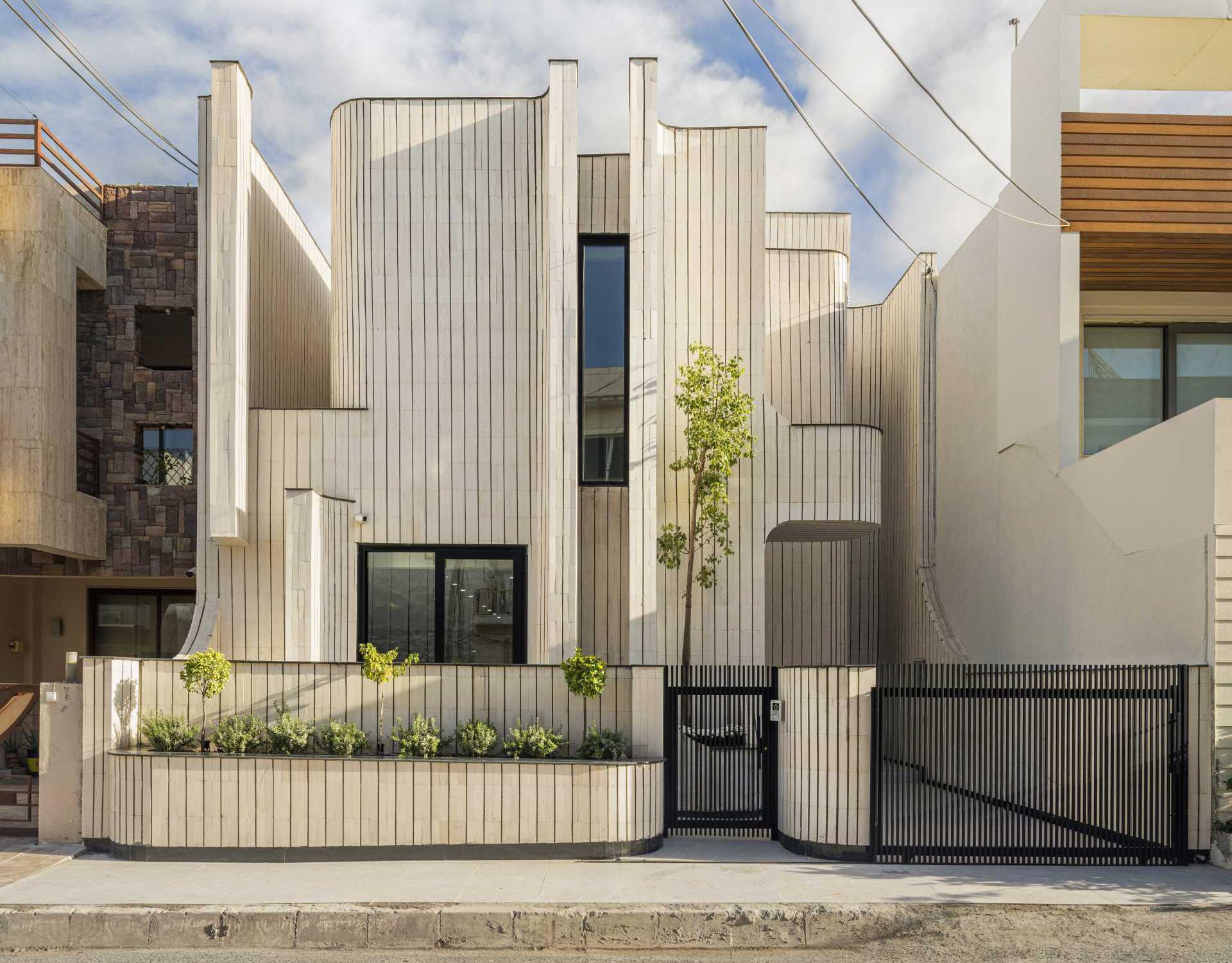 A modern and sculptural house covered in tiles, also has built-in planters.
