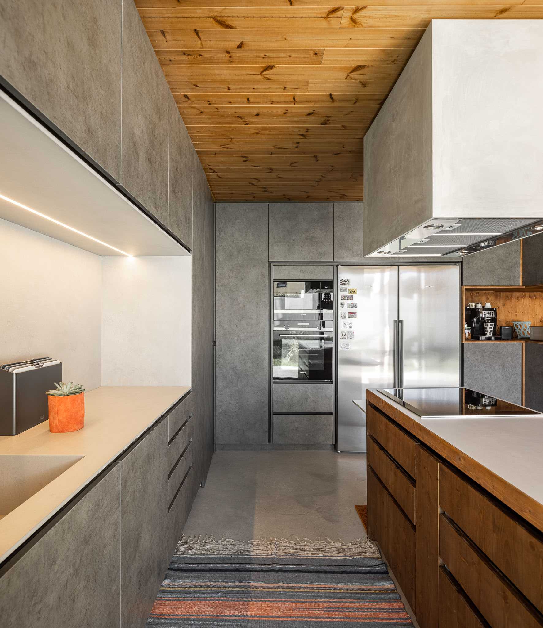 A modern kitchen with a wood ceiling, grey cabinets, and wood island.