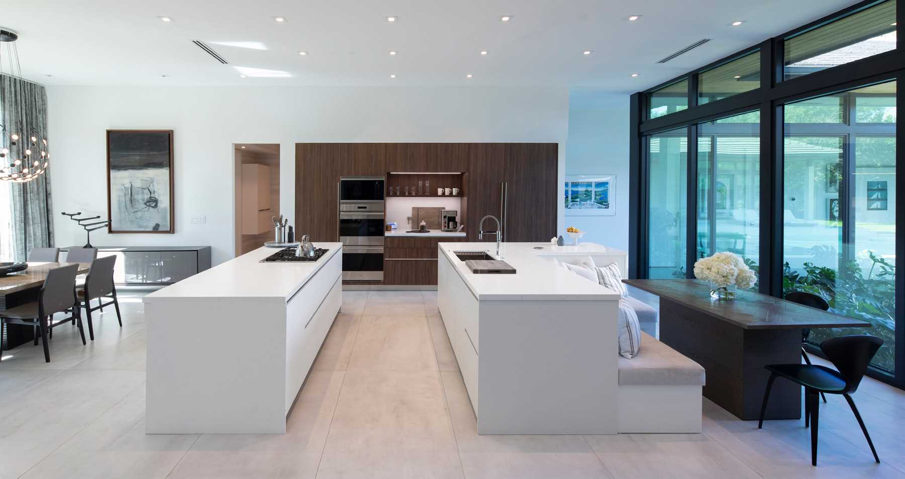 A modern kitchen with two islands. One of the islands drops down to act as banquette seating for the casual dining area.