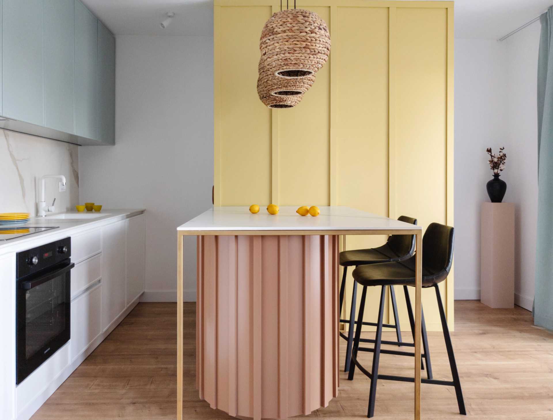 Pastel colors have been used to brighten up this contemporary kitchen, with a yellow accent wall, a curved light pink base for the peninsula, and muted mint green for the upper cabinets. Woven pendant lights add a natural touch to the space.