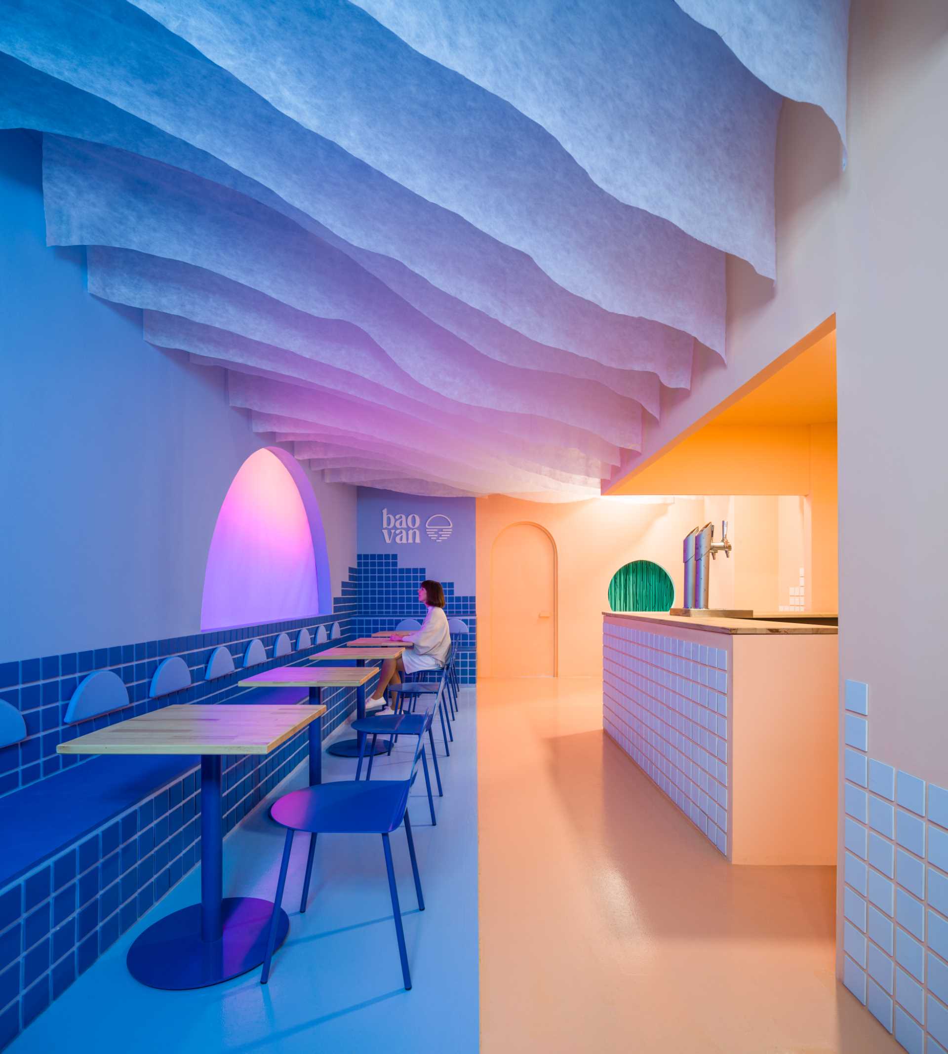 A modern restaurant inspired by a beach sunset, includes a custom light screen that changes colors.