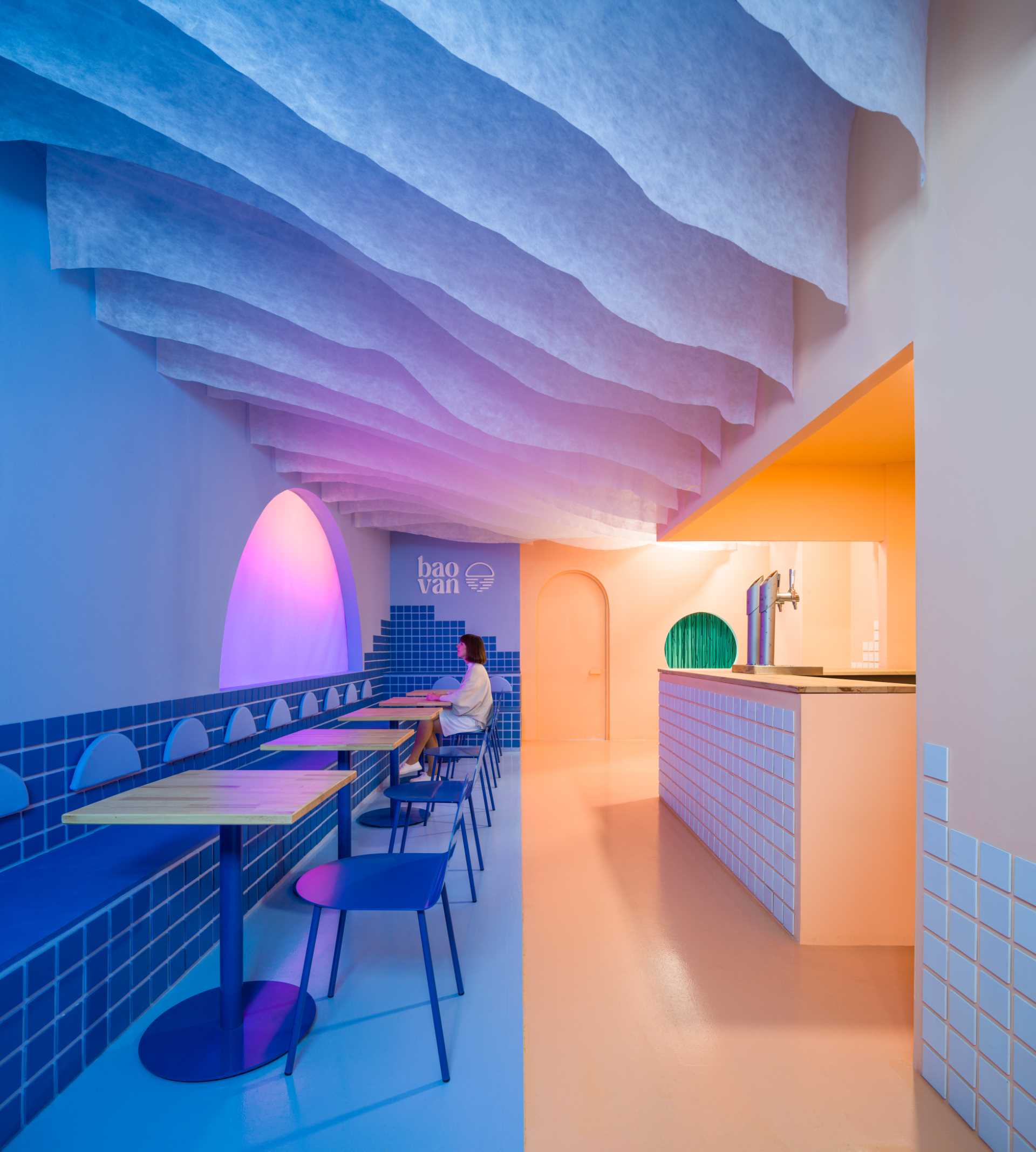 A modern restaurant inspired by a beach sunset, includes a custom light screen that changes colors.