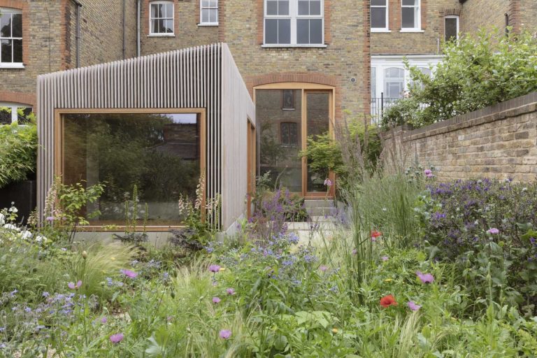 This Home Extension Covered In Vertical Wood Slats Includes A Picture Window Overlooking The Garden
