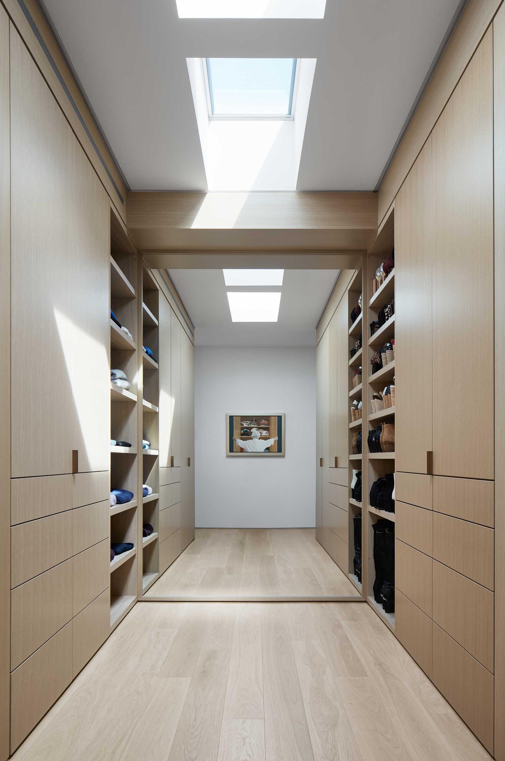 This modern walk-in closet has shoe storage, a large mirror, and skylights.